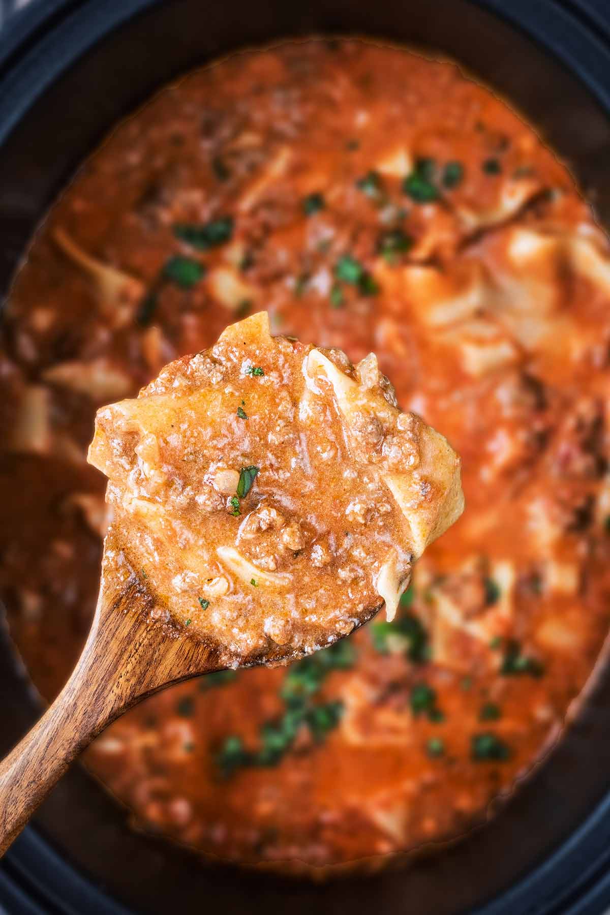 A wooden spoon lifting lasagna soup from a slow cooker bowl.